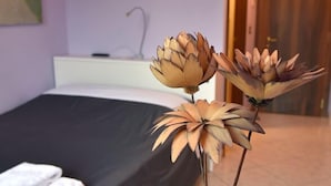 A room with a bed, a blue vase with flowers, and a white table. - Agriturismo Argaland (Parma)