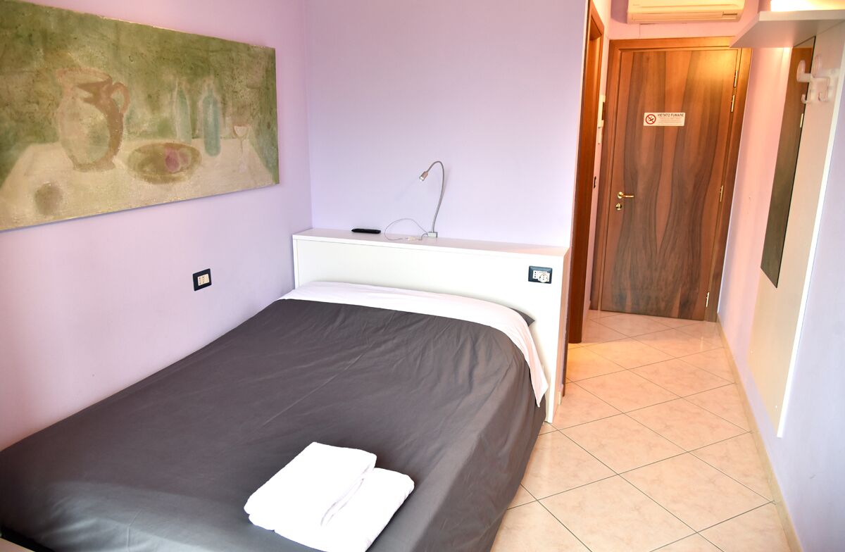 A bedroom with a bed, a nightstand, a painting on the wall, a door, and a sign on the door.
