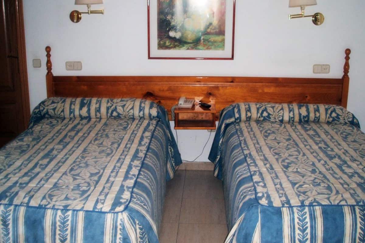 Habitación doble con dos camas, cada una con una colcha estampada, cabecero de madera, lámparas de noche, una mesita con teléfono y un cuadro enmarcado en la pared.