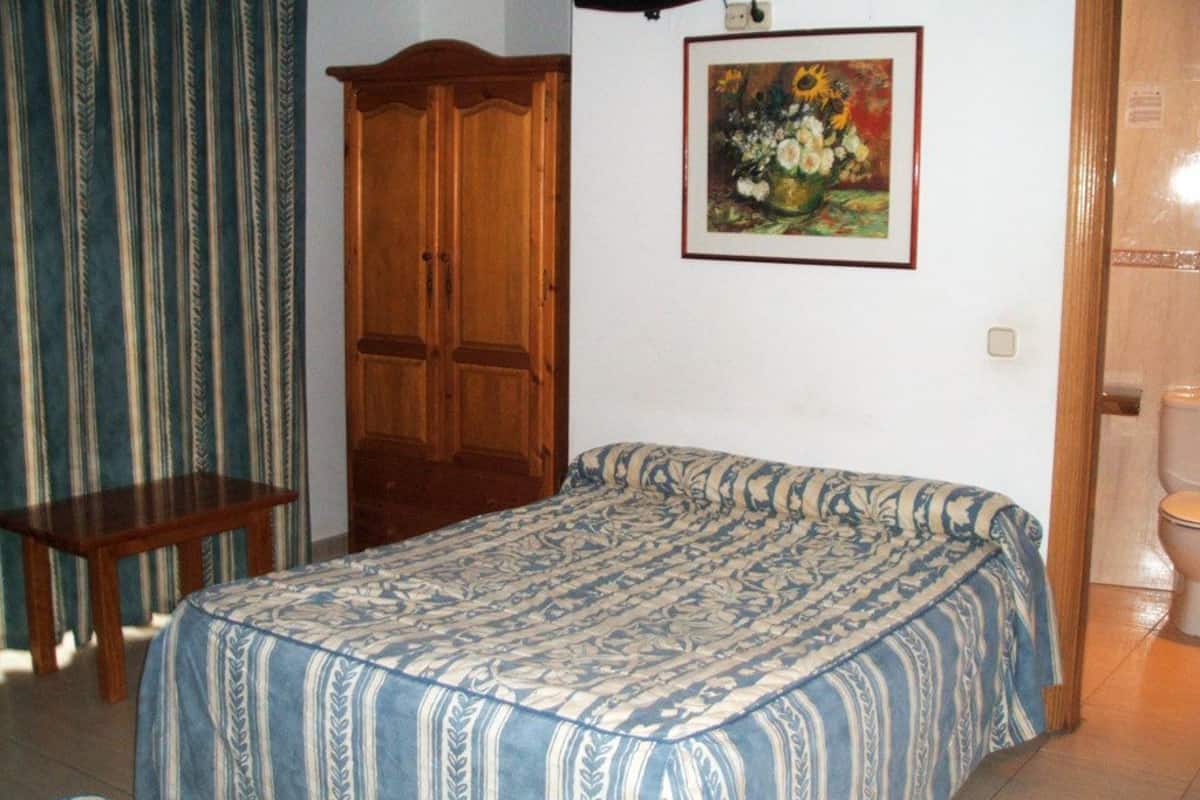 Un dormitorio con cama, un armario de madera, una mesita y un cuadro en la pared.