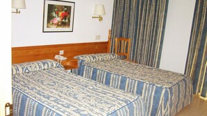 Habitació d'hotel amb dos llits, un panell de capçalera de fusta, una taula de nit, una làmpada, un quadre amb marc i una finestra amb cortines.