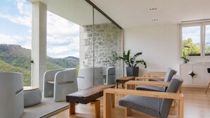 Ein modernes Interieur mit einer Steinwand, großen Fenstern und Blick auf eine gebirgige Landschaft.