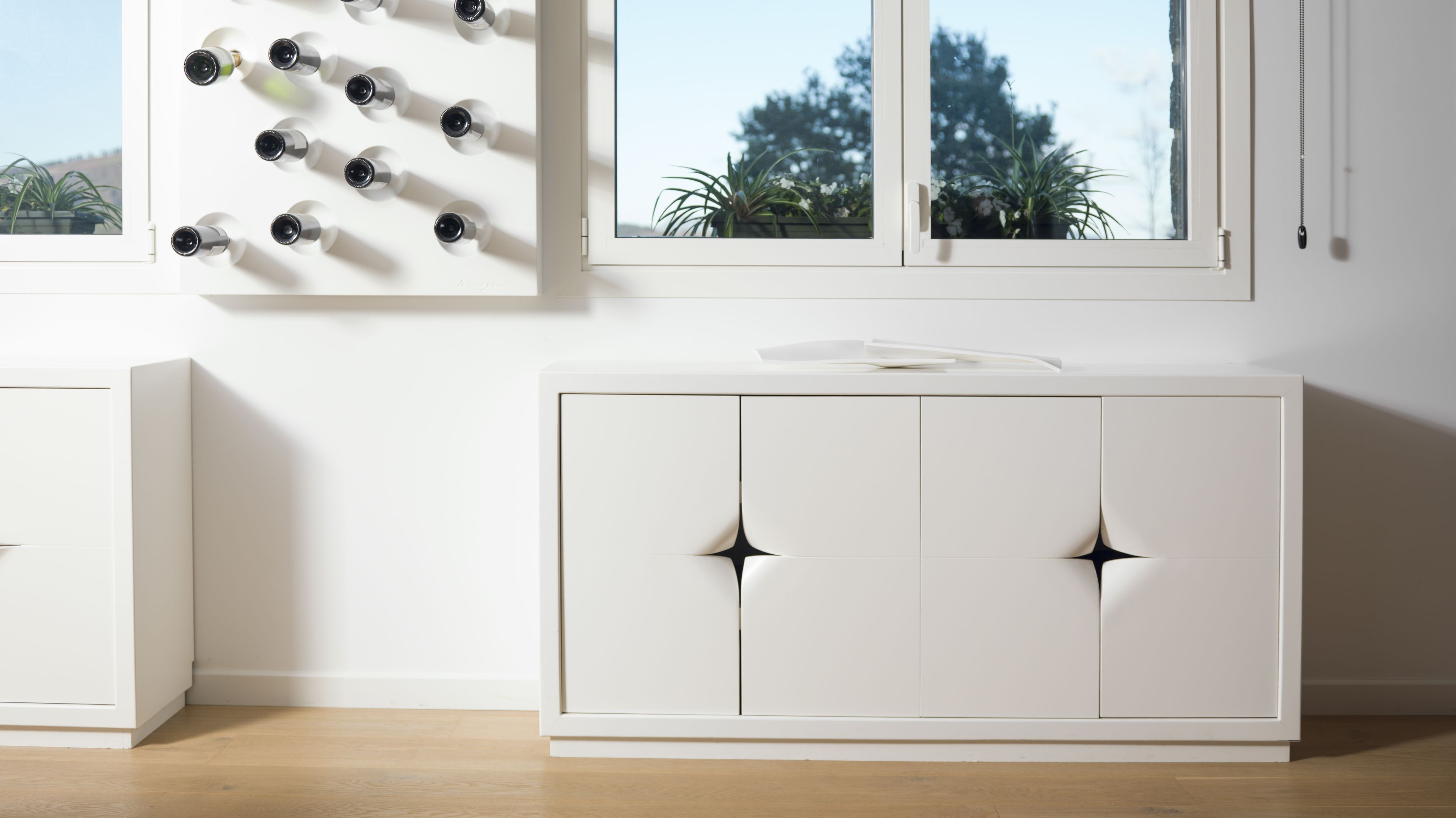 A modern, minimalist room with a white cabinet and a window with multiple cameras.