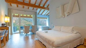 Ein Schlafzimmer mit Bett, Schreibtisch, zwei Stühlen und einem großen Fenster mit Blick auf eine Berglandschaft.