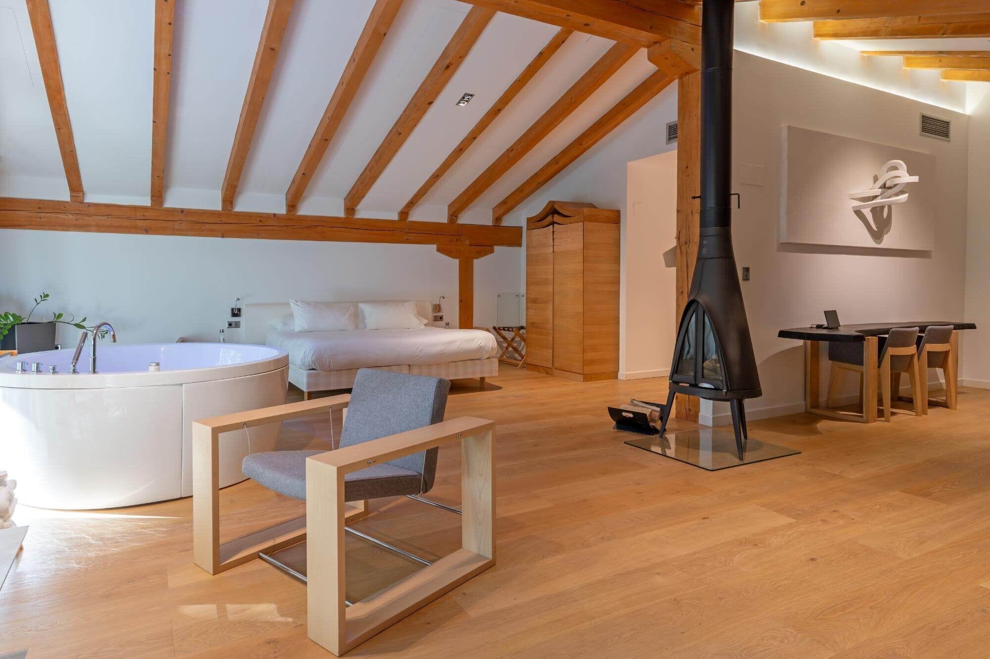 Un dormitorio moderno con una cama grande, techo de madera, un calentador negro y una pequeña mesa con sillas.