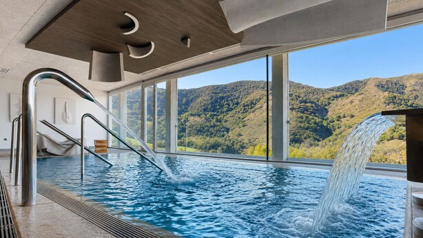 Ein Innenpool mit Blick auf eine Berglandschaft, einem Wasserfall und einem modernen architektonischen Design.