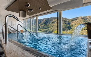 Piscina interior con vistas a un paisaje montañoso, una cascada y un diseño arquitectónico moderno.