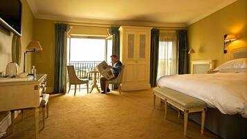 A hotel room with a bed, a desk with a chair, a small table, and a window with curtains.