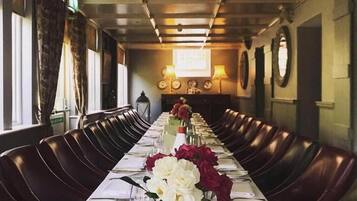 A long dining table set with white tablecloths, red and white flowers, and empty wine glasses.
