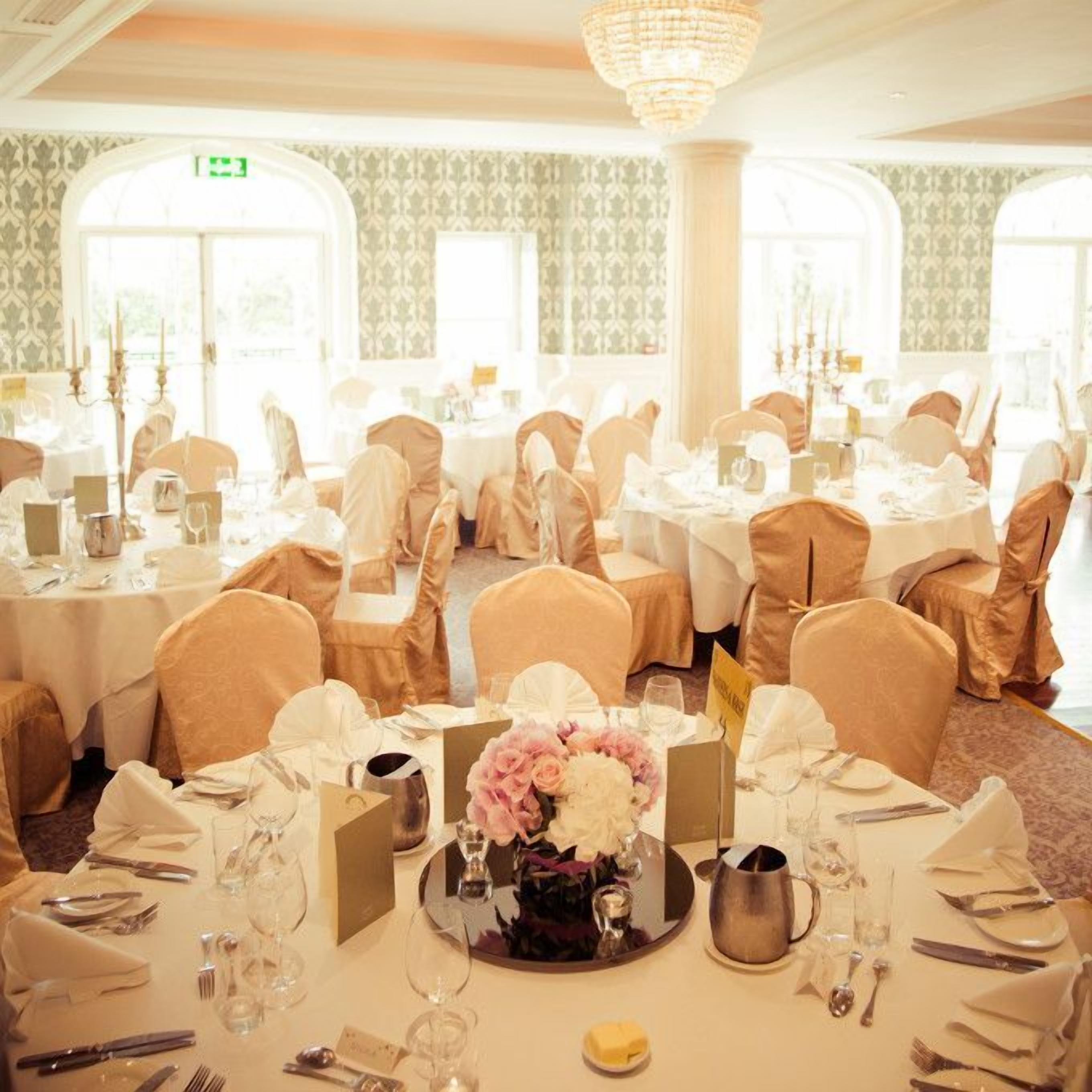 A banquet hall with round tables, white tablecloths, and chairs covered in beige fabric.