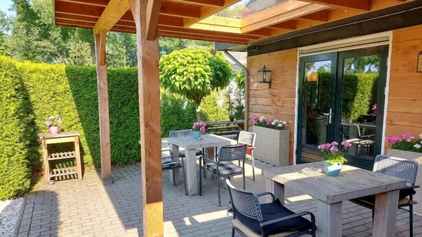 An outdoor patio with wooden tables and chairs, surrounded by a wooden pergola and a hedge. - Guesthouse Lazey (Voorthuizen)
