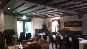 A hotel lobby with a dining area, sofas, and a 'Family Garden' sign. - Guesthouse Lazey (Voorthuizen)