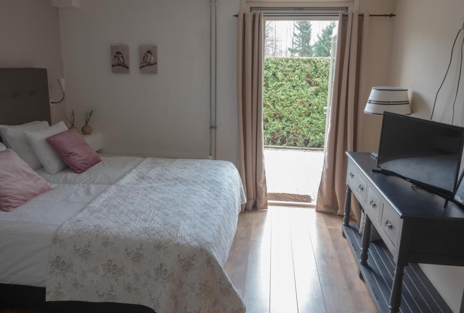 A bedroom with a bed, a dresser, a TV, and a window with curtains.