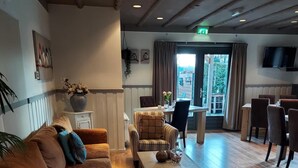 A spacious lobby with wooden flooring, striped armchairs, a sofa, and a dining area with tables and chairs. - Guesthouse Lazey (Voorthuizen)