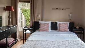 A bedroom with a large bed, bedside tables, a lamp, and a view of greenery outside. - Guesthouse Lazey (Voorthuizen)