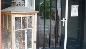 A black door with a white frame, a small wooden lantern, and a doormat. - Guesthouse Lazey (Voorthuizen)
