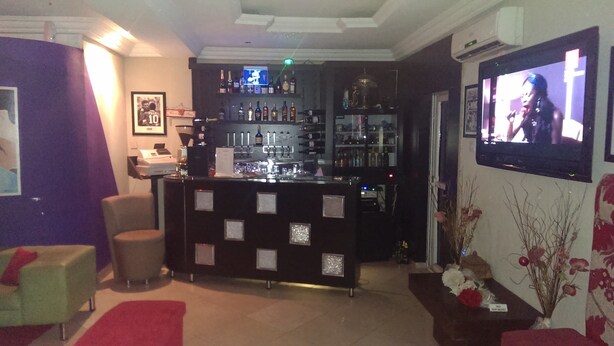 A bar area with a counter, shelves of bottles, and a television screen. - Dcove Hotel & Suites (Lagos)