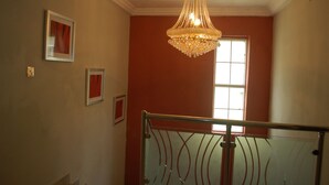 A staircase with a glass railing, a chandelier, and framed pictures on the walls. - Dcove Hotel & Suites (Lagos)