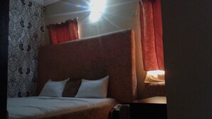 A hotel room with a large bed, a headboard, and a nightstand with a lamp. - Dcove Hotel & Suites (Lagos)