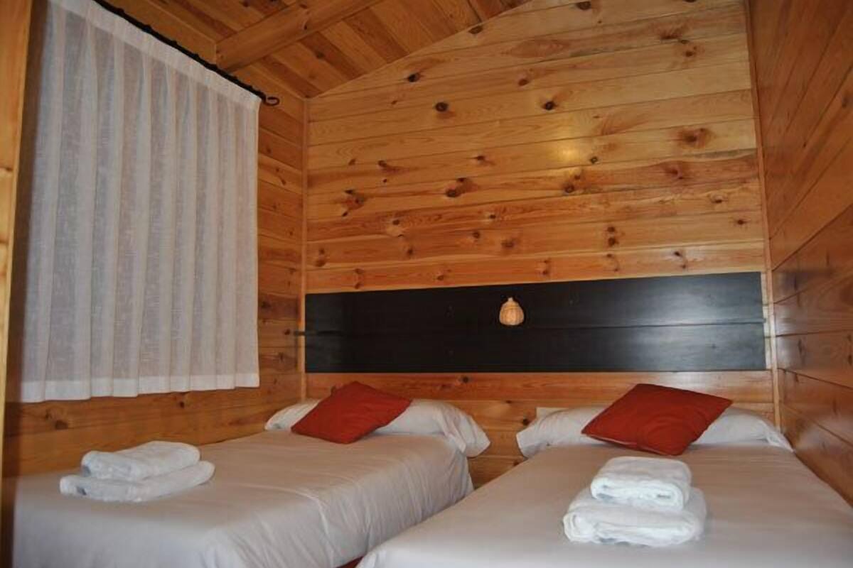 A wooden cabin room with two beds, each with a pillow and a rolled towel.