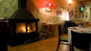 A cozy dining area with a stone fireplace, wooden furniture, and a television mounted on the wall. - Cabañas de Javalambre (Camarena de la Sierra)