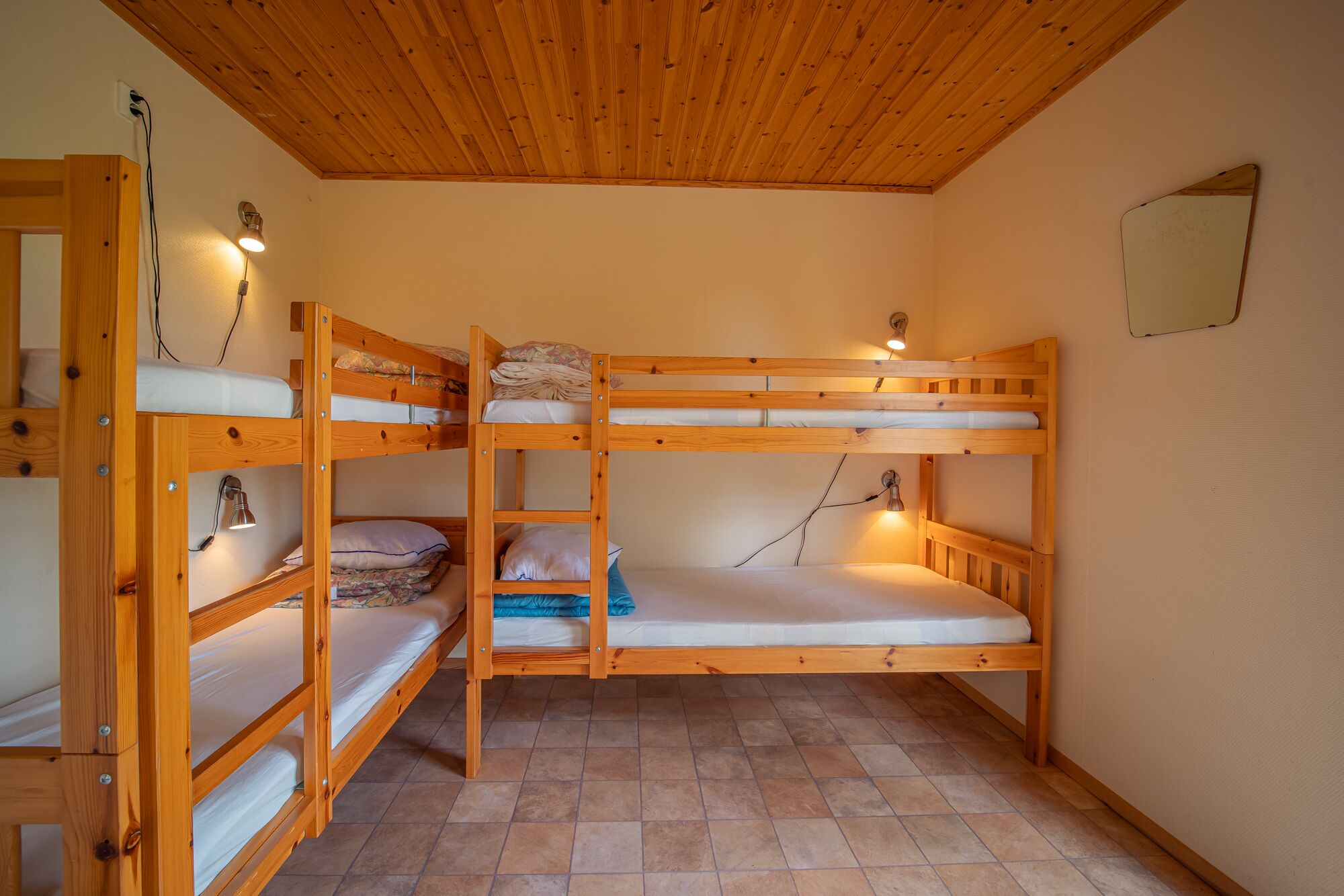 Een slaapkamer met stapelbedden van hout, elk met een bedlampje.