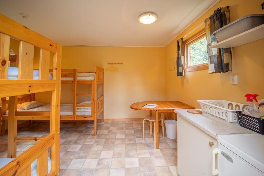 Habitació compacta amb llits superposats, una taula petita, un refrigerador i una finestra amb cortines.