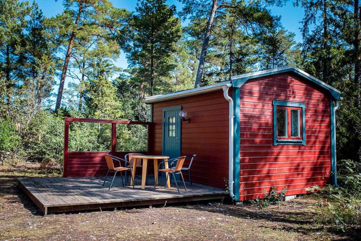 Eine kleine rote Holzhütte mit einer Holzterrasse und zwei Stühlen.