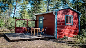 Une petite cabane rouge avec une terrasse en bois et deux chaises.