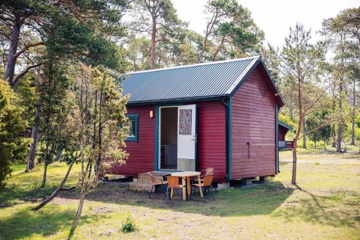 Eine kleine rote Holzhütte mit einem Metalldach, einem Holztisch und Stühlen davor.