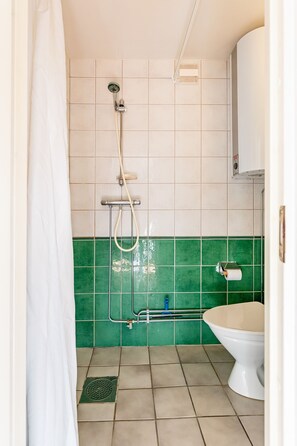 A bathroom with a shower, toilet, and green-tiled walls.