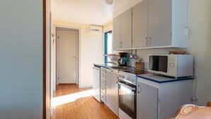 Une cuisine de taille réduite avec des meubles blancs, un four à micro-ondes, un four traditionnel et une chaise en bois.