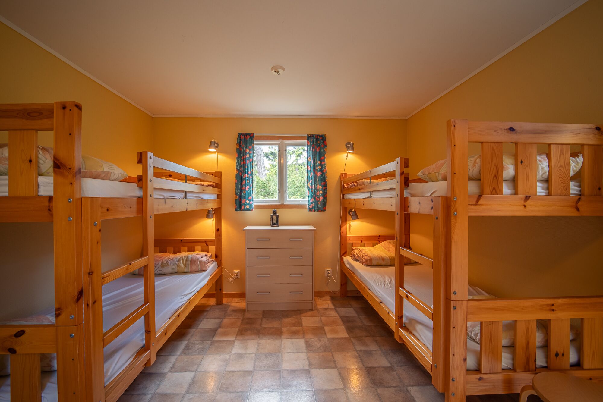 A dormitory room with bunk beds, a small desk, and a window with curtains.