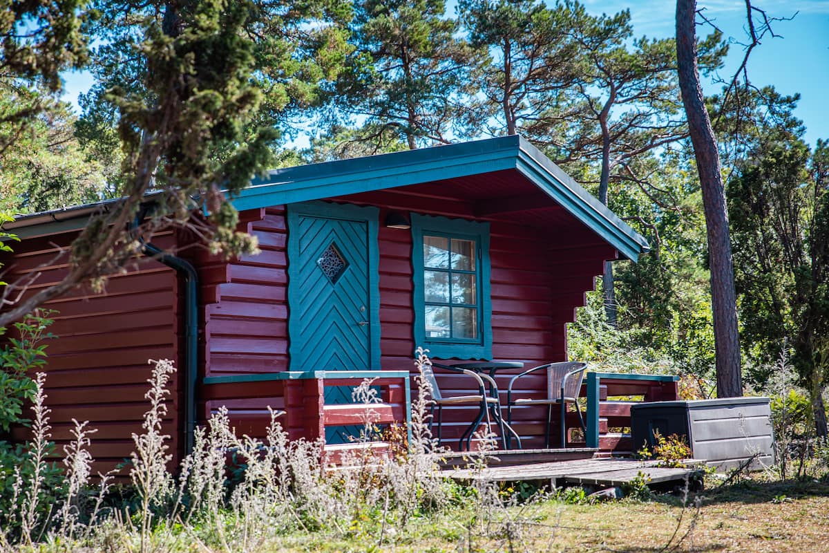 Eine Hütte mit roter Fassade und blauen Verzierungen, eine Veranda mit einer Bank und ein kleines Gartenhaus.