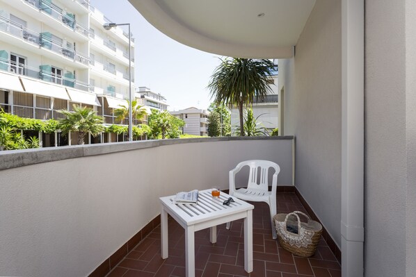 A balcony with a white table, a white chair, and a woven basket. - Residenza Levante (Riccione)