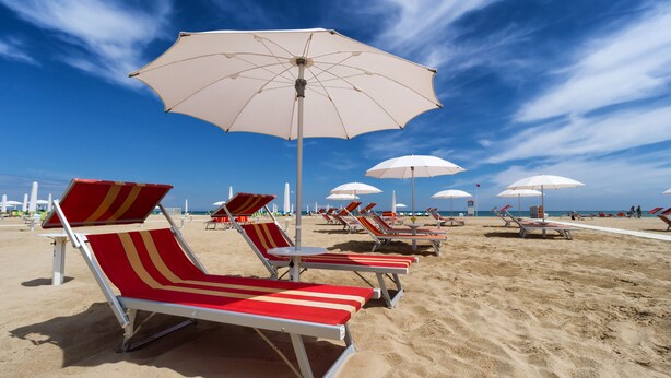 A beach with red and white striped lounge chairs and white umbrellas. - Residenza Levante (Riccione)