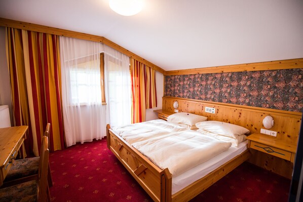A wooden bed with white linens, a wooden nightstand, a wooden desk, and a chair.