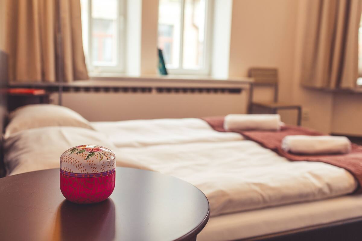 A neatly made bed with white linens and a pink decorative item on a round table.