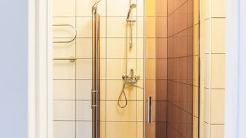 A glass-enclosed shower with a white base, tiled walls, and a wooden floor.