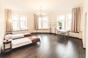Hotellihuone, jossa on kaksi sänkyä, ruokapöytä, tuoleja, kattokruunu ja suuret ikkunat, joissa on verhot.