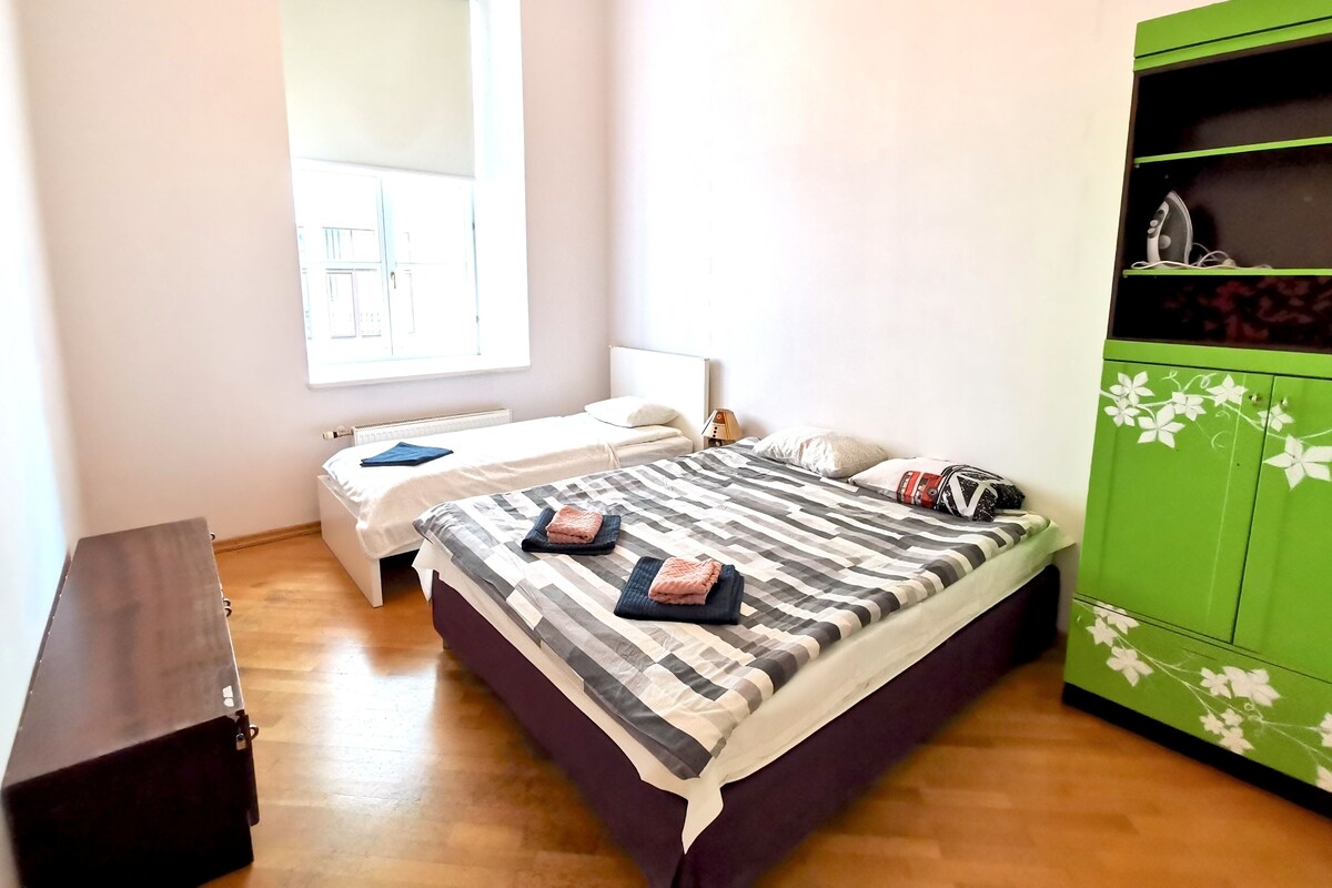 Ein Schlafzimmer mit einem großen Bett, einem grünen Kleiderschrank, einem Fenster und einer Heizung.