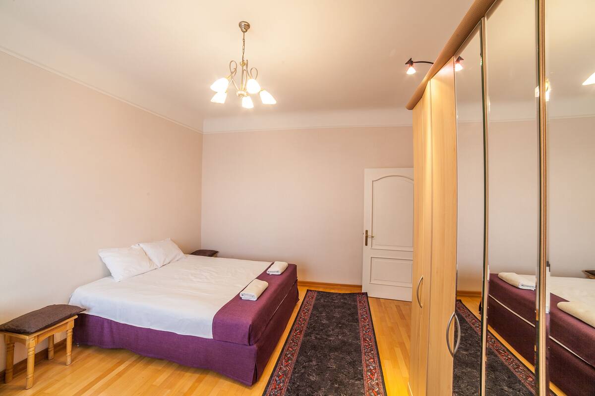 A bedroom with a bed, a bench, a mirror, and a ceiling light.