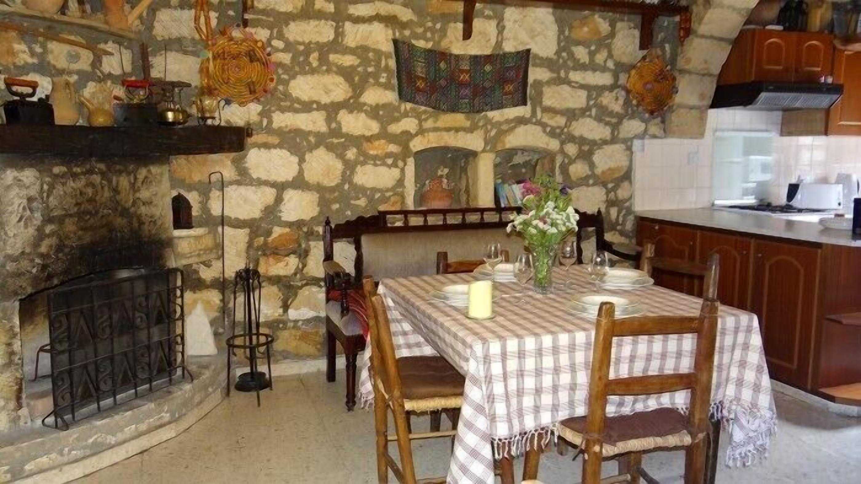 A rustic dining area with a stone wall, a fireplace, and a kitchen area with wooden cabinets.