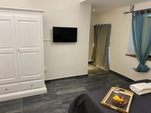 A room with a bed, a TV mounted on the wall, a wardrobe, and a tray with fruits and a bottle. - Agriturismo Il Casolare (Poppi)