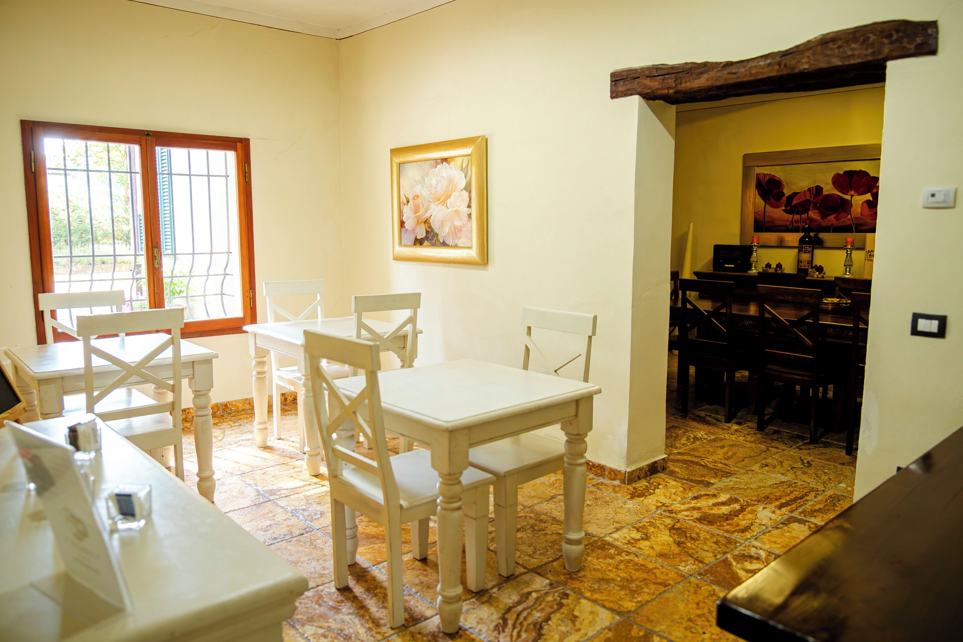 A dining area with a table and chairs, a painting on the wall, and a kitchen in the background.