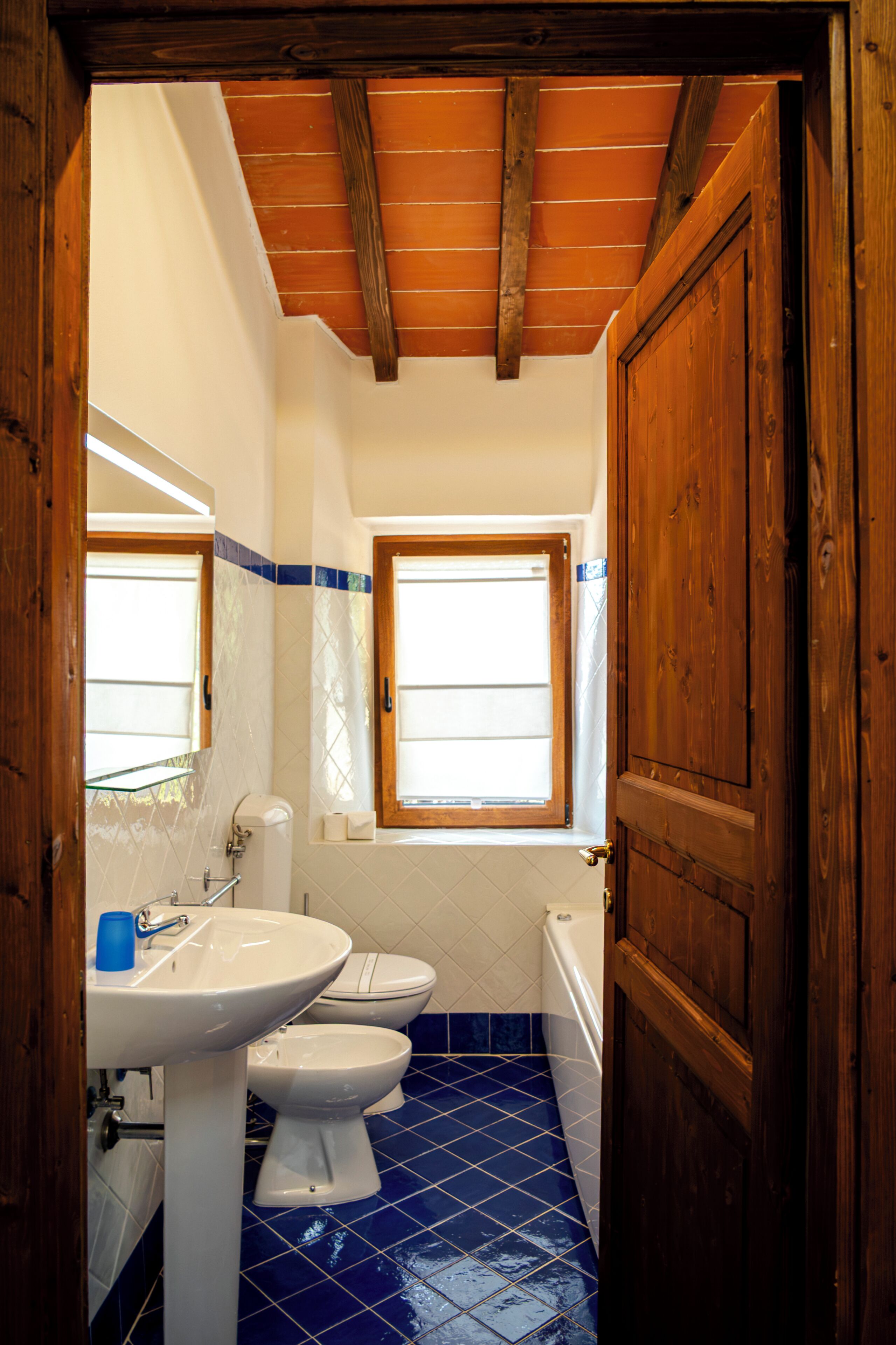A bathroom with a wooden ceiling, a window, a sink, a toilet, and a bathtub.