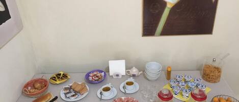 Un bufé de desayuno con diversos alimentos, utensilios y un cuadro de flores en la pared.