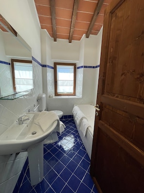 Un baño con lavamanos, inodoro y bañera, vigas de madera en el techo y una ventana.