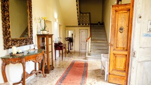 A grand staircase leading to a second floor, a wooden door with a brass handle, and a marble floor with a red and blue patterned rug. - Agriturismo il Casolare - Villa Vettori (Poppi)