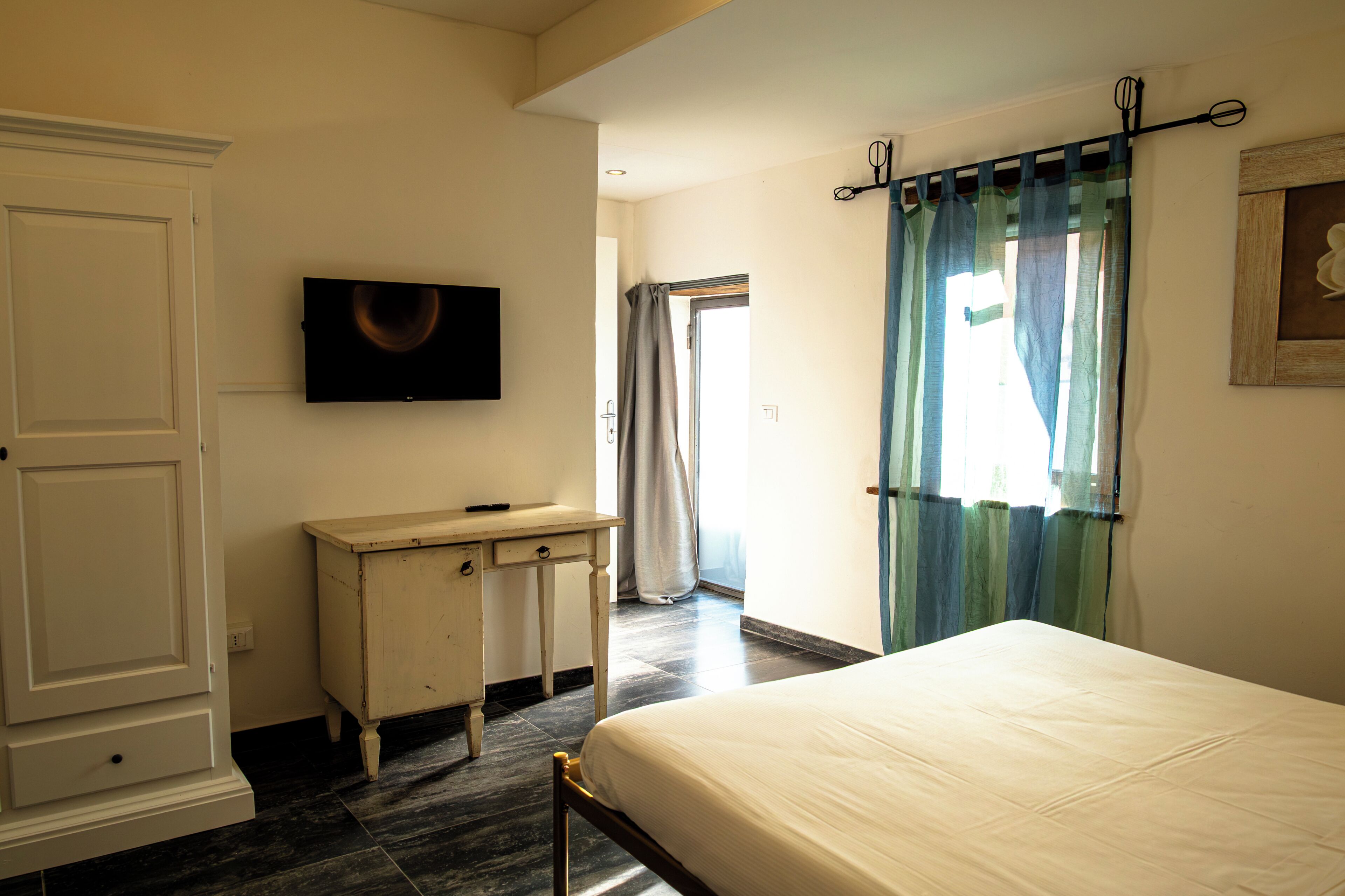 Un dormitorio con cama, escritorio, televisor y ventana con cortinas.
